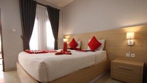 A hotel room with a large bed, two bedside tables, a wooden headboard, and a window with curtains. - Tom Guest House (Kuta)