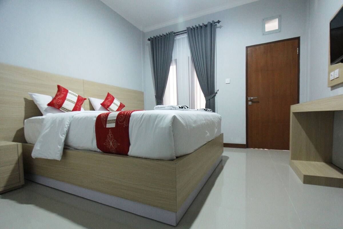 Quarto de hotel moderno com cama de madeira, mesa de cabeceira, televisão integrada e guarda-roupa.
