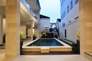 A courtyard with a rectangular pool, potted plants, and a staircase leading to an upper level. - Tom Guest House (Kuta)
