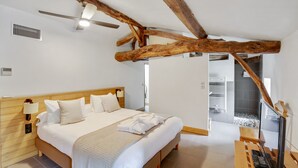A bedroom with a wooden bed, a ceiling fan, and a view of a tiled bathroom. - Logis DE Valandraud (Saint-Etienne-De-Lisse)