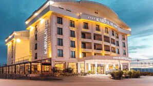 Un hotel de varios pisos con un llamativo letrero de "KARPALAS", con balcones y una entrada bien iluminada.