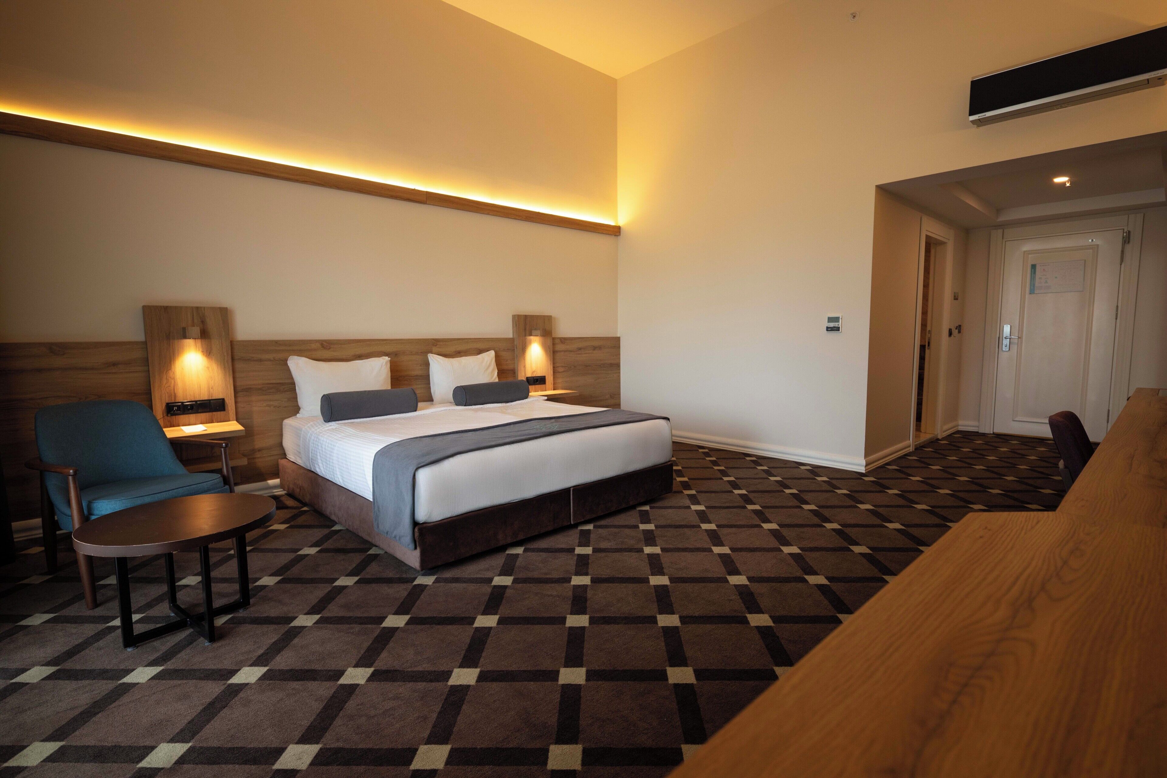 A hotel room with a bed, a desk, a chair, and a check-in counter.