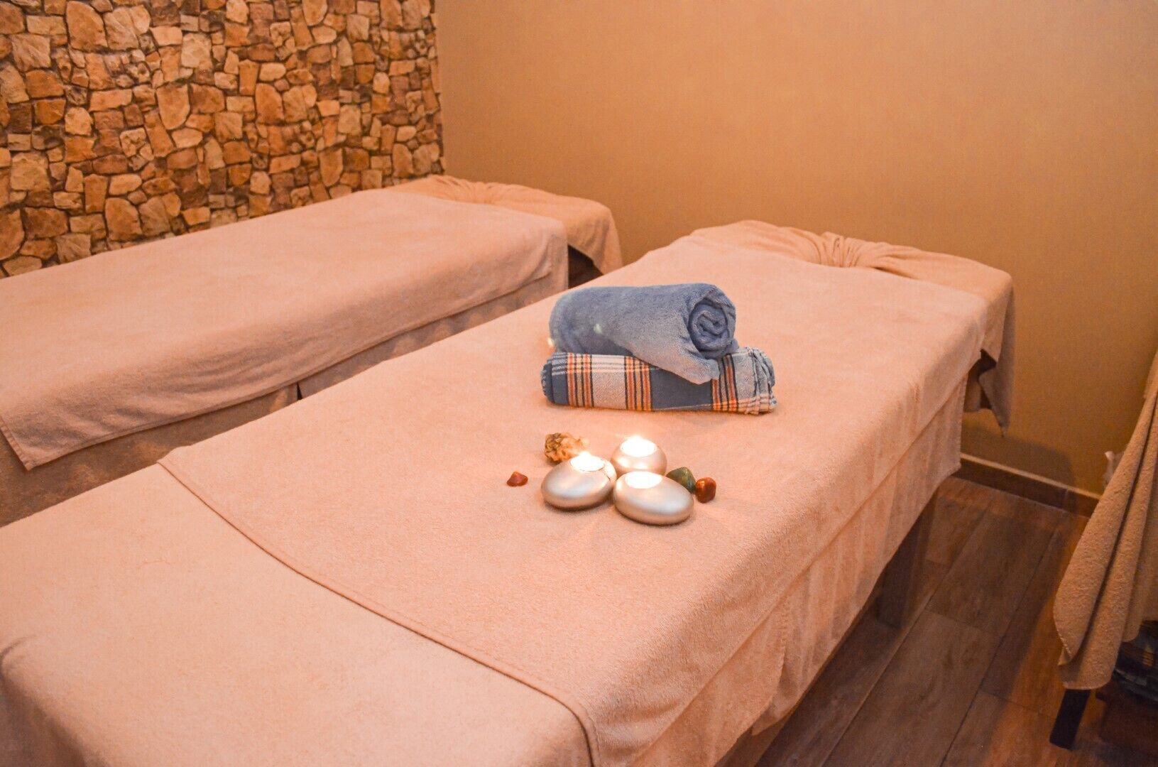 A massage room with two massage tables, a stone wall, and a small arrangement of stones and candles.