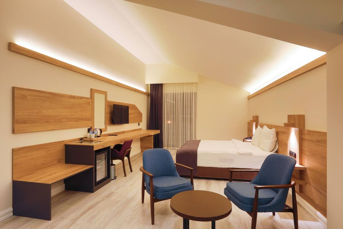 Une chambre d’hôtel moderne équipée d’un lit, d’un bureau, de deux chaises, d’une petite table et d’un téléviseur.