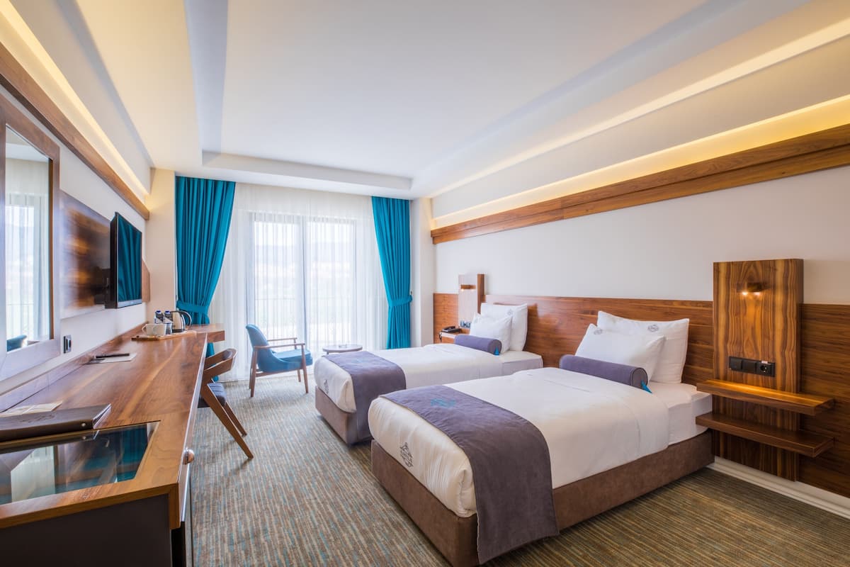 Une chambre d’hôtel avec deux lits, un bureau, une chaise, une télévision et une tête de lit en bois.