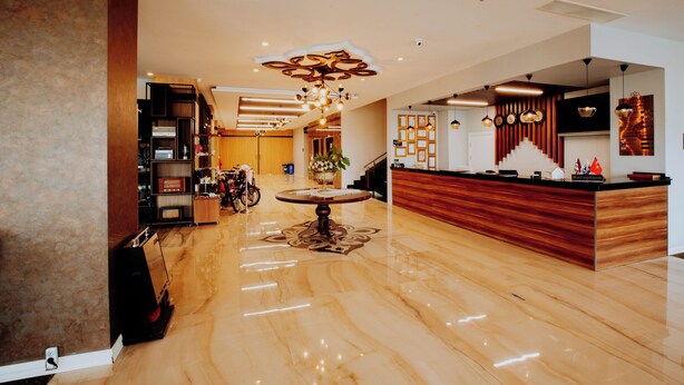 Un moderno hall de hotel con mostrador de recepción, una mesa redonda con un centro de mesa floral y una escalera que conduce a los pisos superiores.