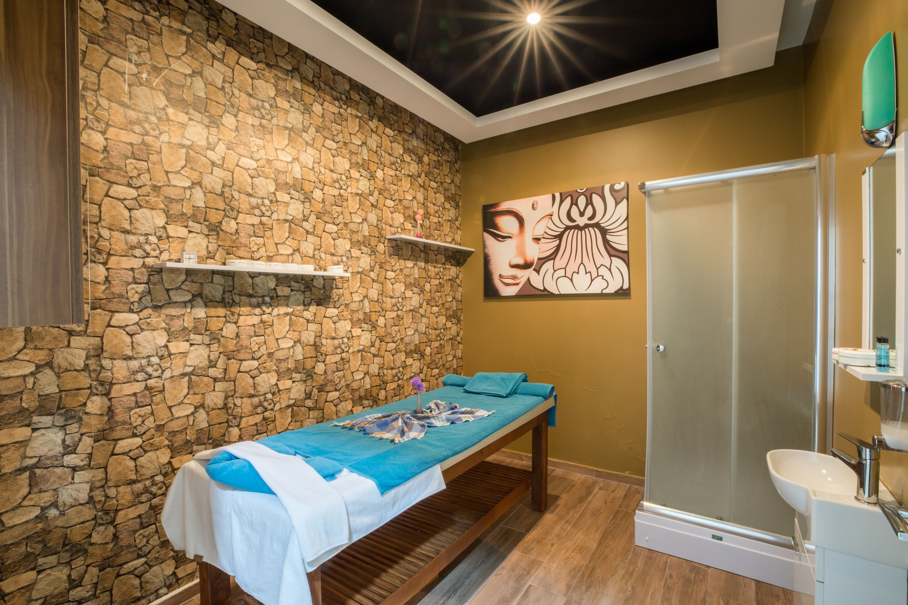 Un cuarto de spa con pared de piedra, una camilla de masaje, cabina de ducha de vidrio y estante empotrado.