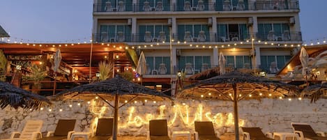 A hotel with multiple balconies, outdoor seating with umbrellas, and a stone wall.