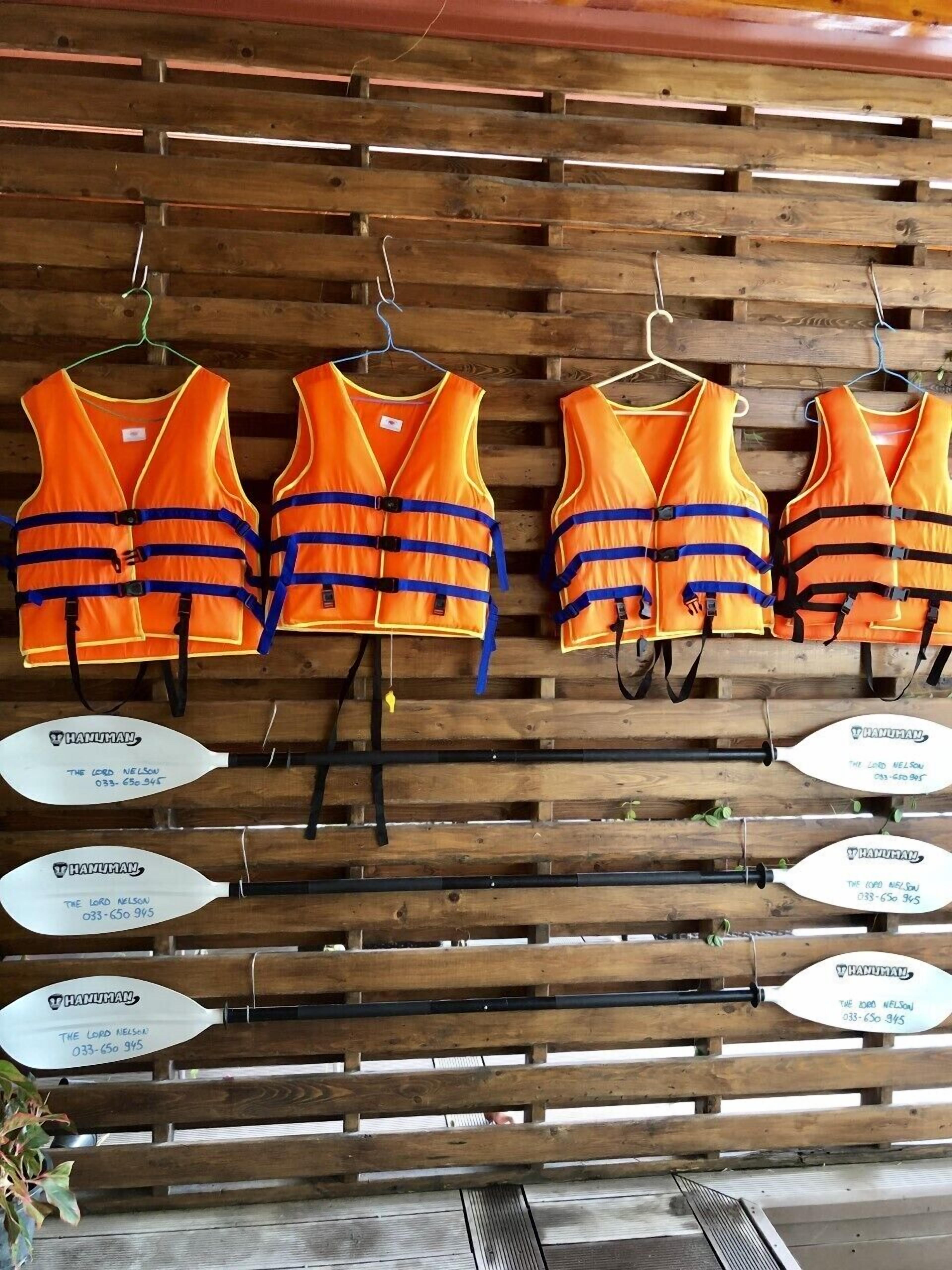 Chalecos salvavidas naranja colgados en una pared de madera con la información de contacto para 'The Lord Nelson' mostrada debajo.