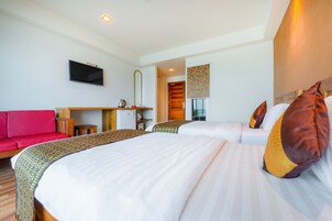 Habitación de hotel con dos camas, un sofá rojo, un televisor, un escritorio con una tetera y una puerta de madera.