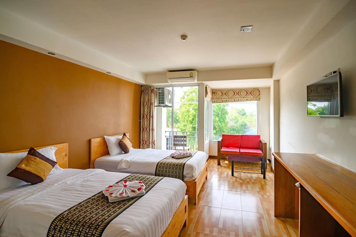 A hotel room with two beds, a red chair, a wooden desk, and a TV on the wall.