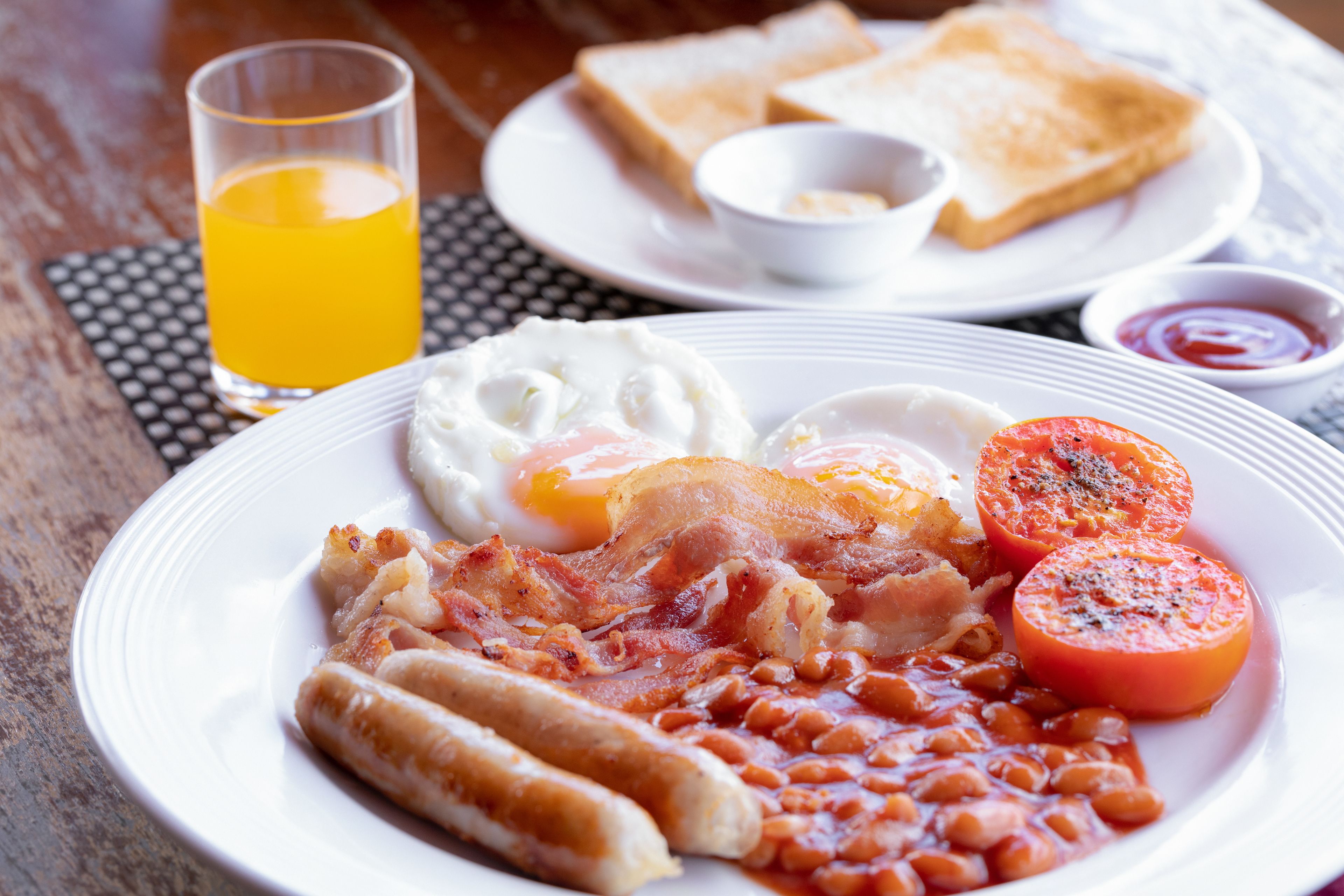 Um prato de comida de café da manhã com ovos, bacon, linguiça, feijão e tomate.