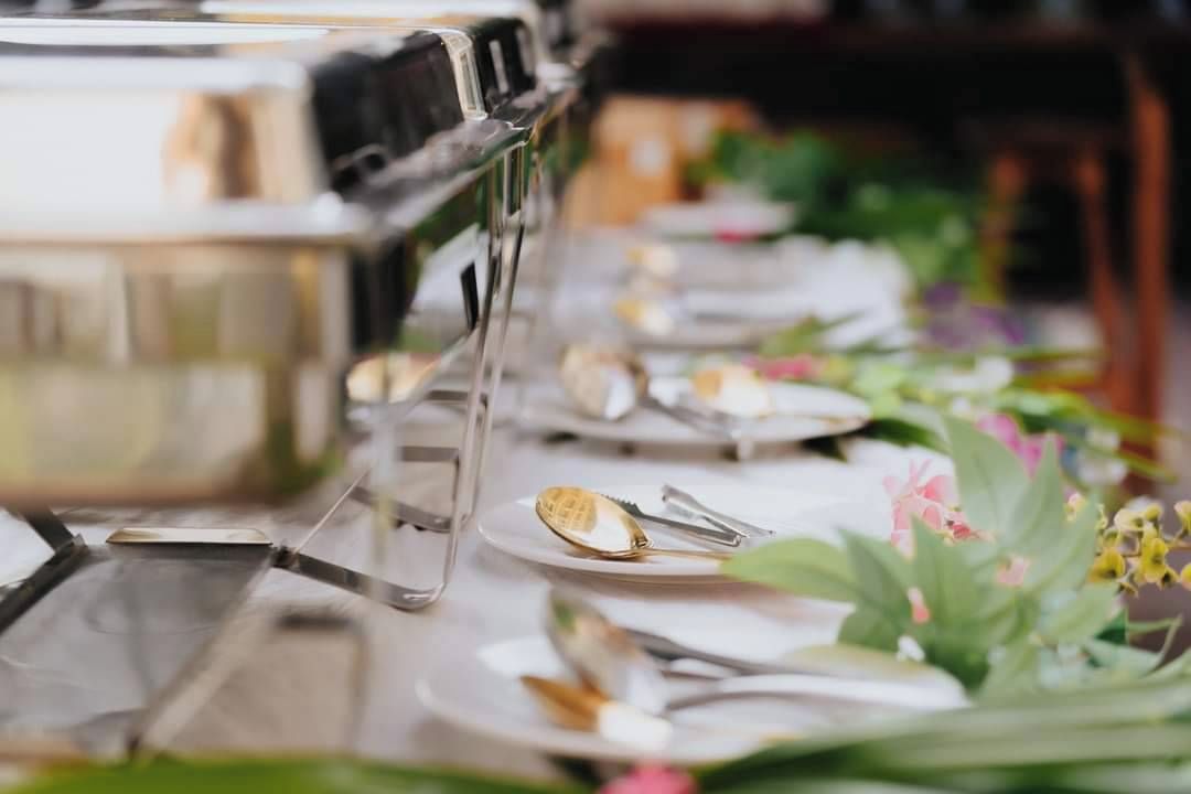 Una mesa larga con un bufé, vajilla de plata y cubiertos.