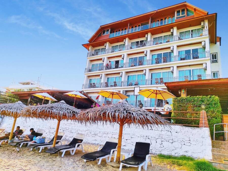 A hotel with multiple balconies, outdoor seating with umbrellas, and a beach area with sun loungers.
