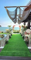 Un pasillo nupcial con césped artificial, decoración floral y vista al mar.
