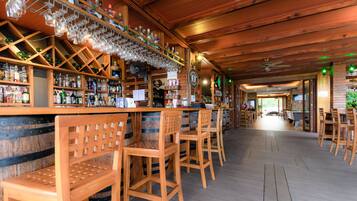 A bar area with wooden chairs, a bar counter with bottles and glasses, and a wooden ceiling.
