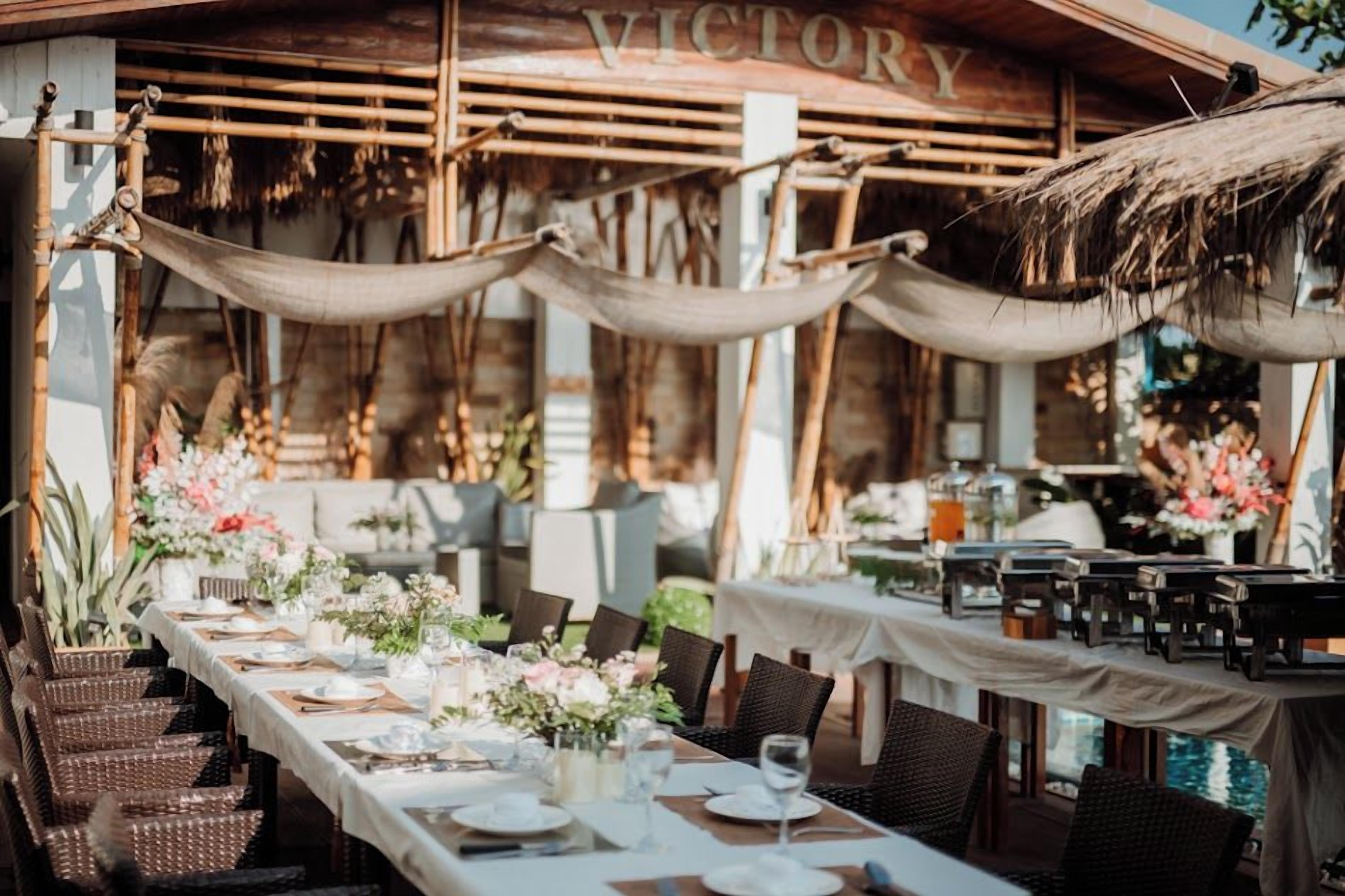 An outdoor dining area with a long table set for a meal, surrounded by wicker chairs.