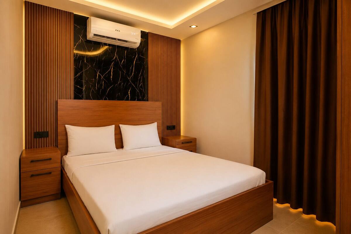 A bedroom with a wooden headboard, white bedding, a nightstand, a drawer, and a wall-mounted air conditioner.