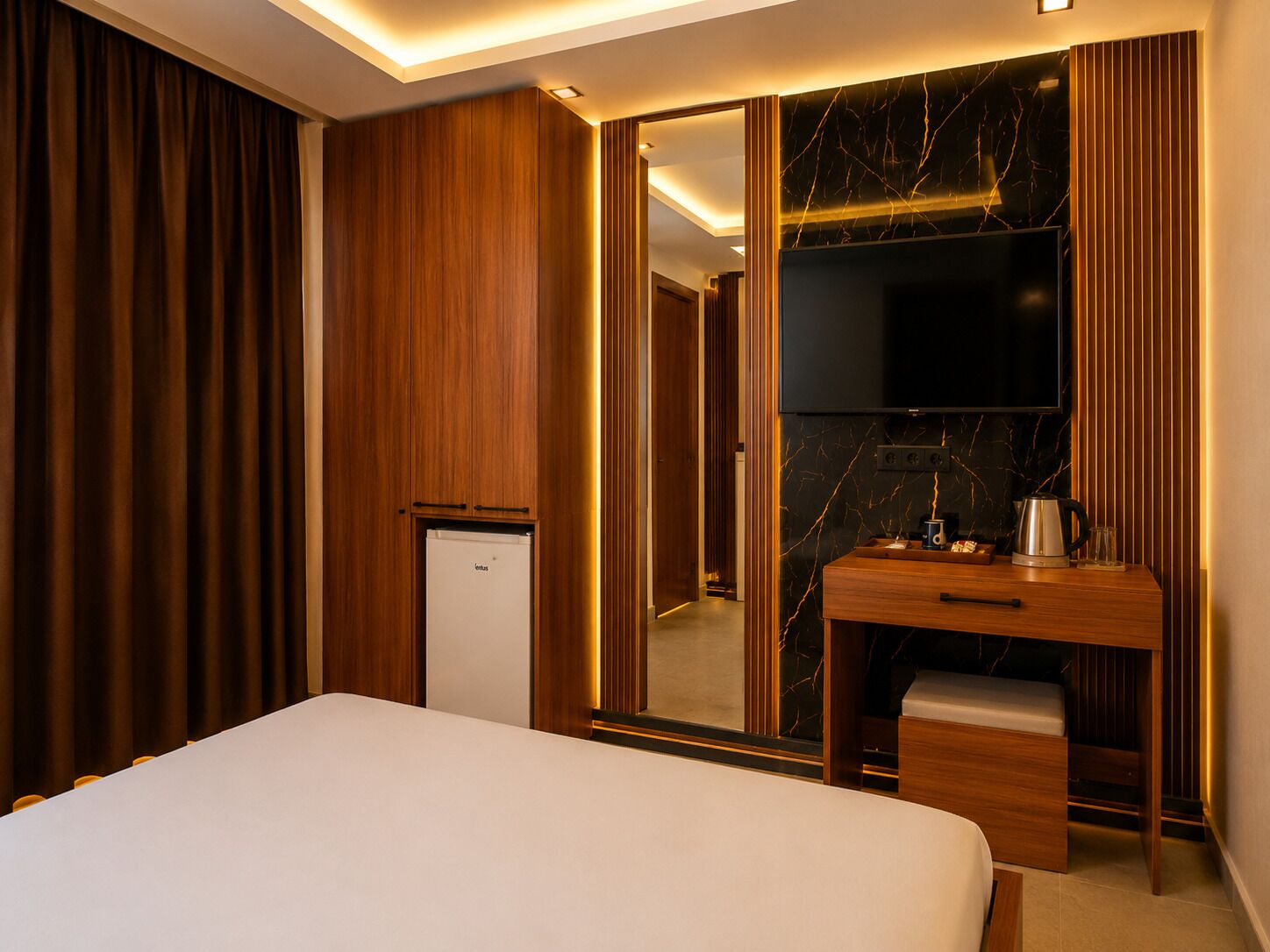 Une chambre d’hôtel avec un lit, un bureau en bois, un miroir et un mini-bar.