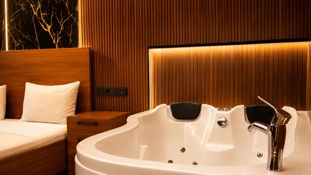 A modern bathroom with a large bathtub, wooden paneling, and a bedside table. - Palmiye Suit (Istanbul)