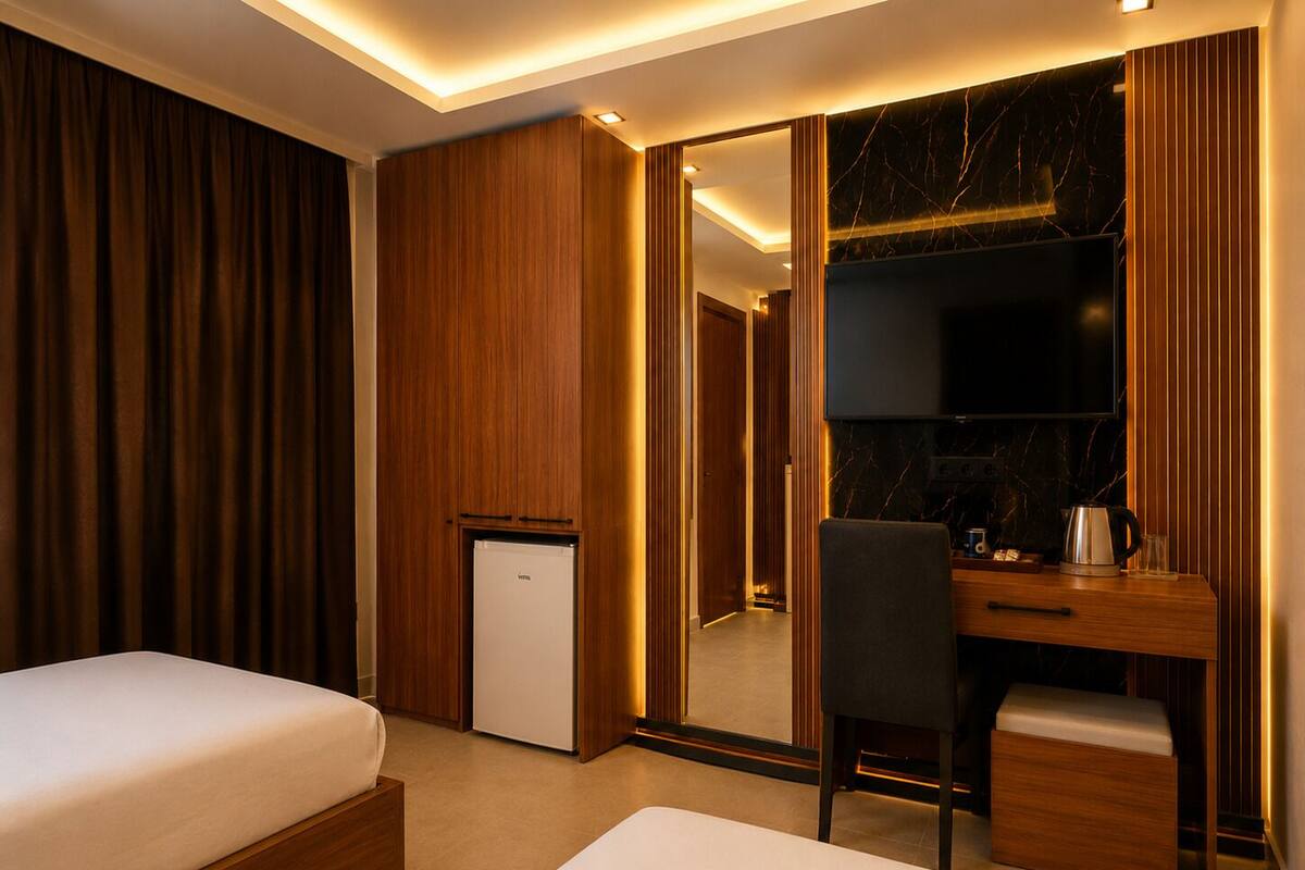 A hotel room with a bed, a desk, a chair, a small refrigerator, and a mirror.