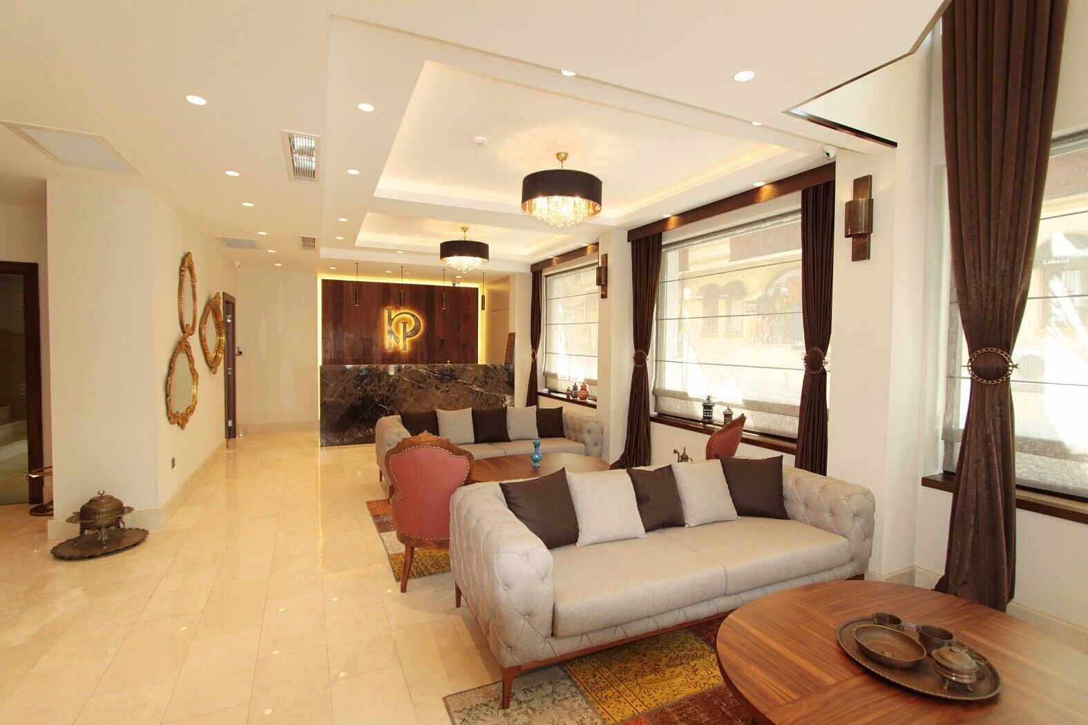 A spacious living area with a sofa, a coffee table, and a dining table set for four. A reception desk with a marble countertop and a logo is visible in the background.