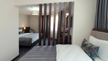 Ein Hotelzimmer mit einem großen Bett, einem kleineren Bett, einer Holzwand, einem Schreibtisch mit Lampe und Blick auf den Flur.
