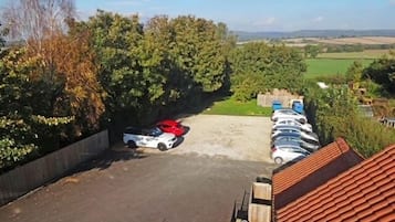Un aparcamiento con varios coches, rodeado de árboles y vistas al campo.
