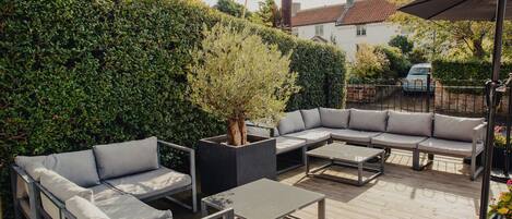 Un patio al aire libre con un sofá modular, una mesa de centro y un árbol en maceta.