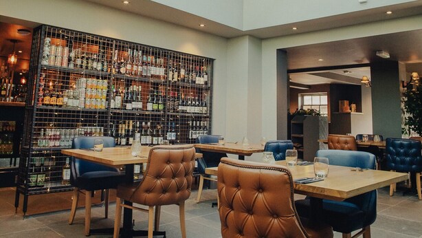 A restaurant with a high ceiling, a glass skylight, and a chandelier. Tables and chairs are arranged for dining. - Plum and Partridge Inn (York)