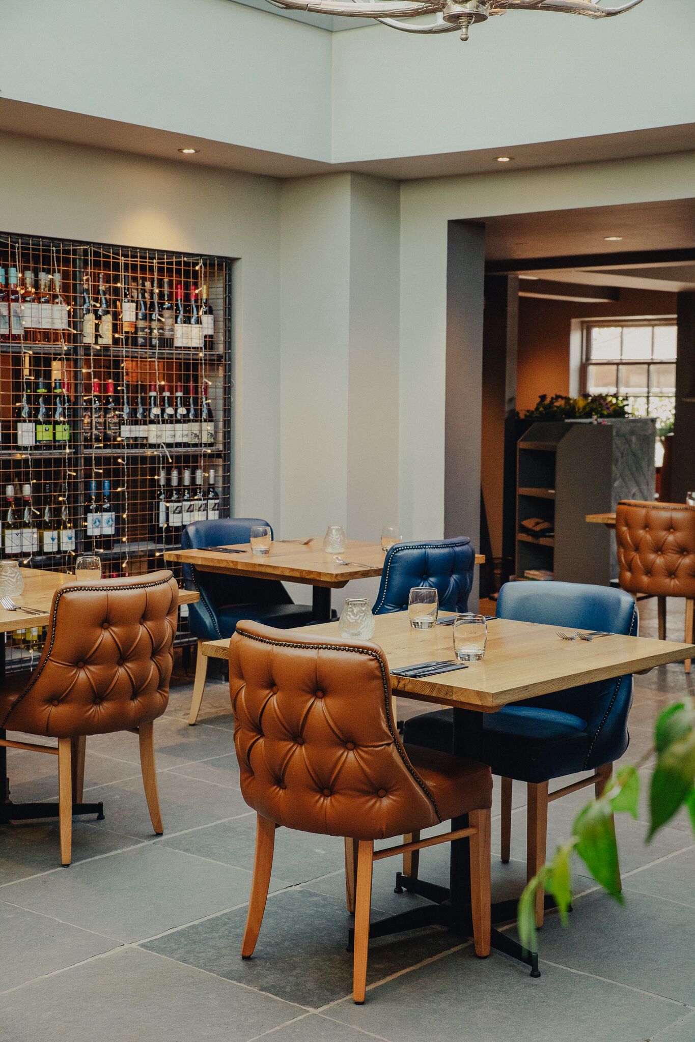 A restaurant with leather chairs, wooden tables, and a wine rack in the background.