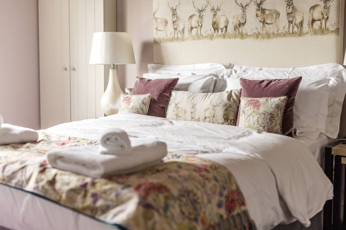 A neatly made bed with floral bedding, a white headboard, and decorative pillows.