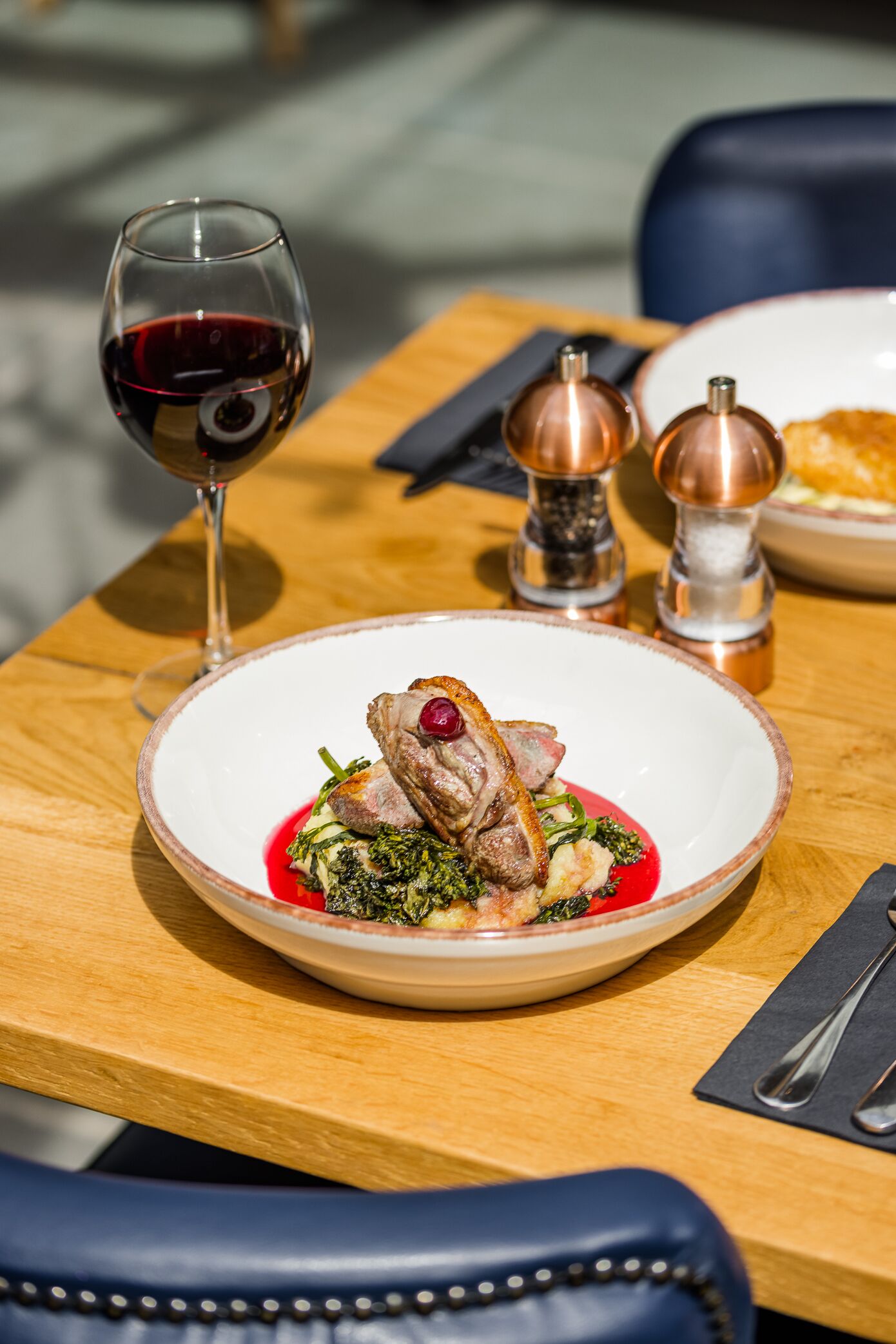Una mesa de comedor con un plato de comida, una copa de vino tinto y dos saleros.