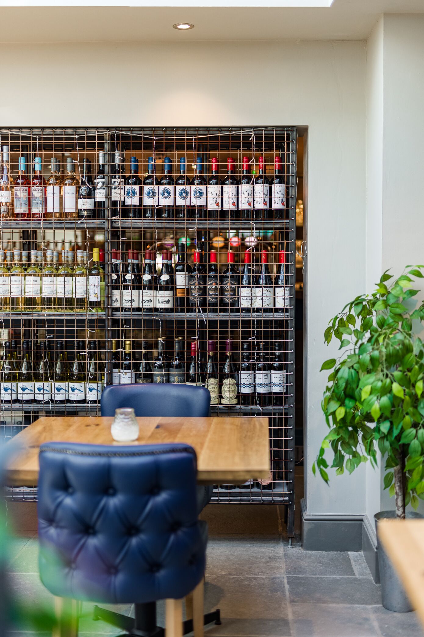 A restaurant interior with a wine rack, a wooden table, and blue chairs.