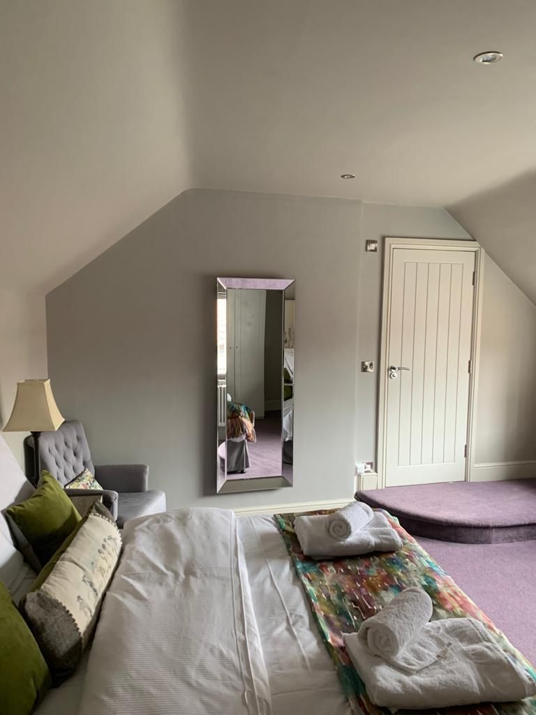 A bedroom with a large bed, a chair, a mirror, and a door.