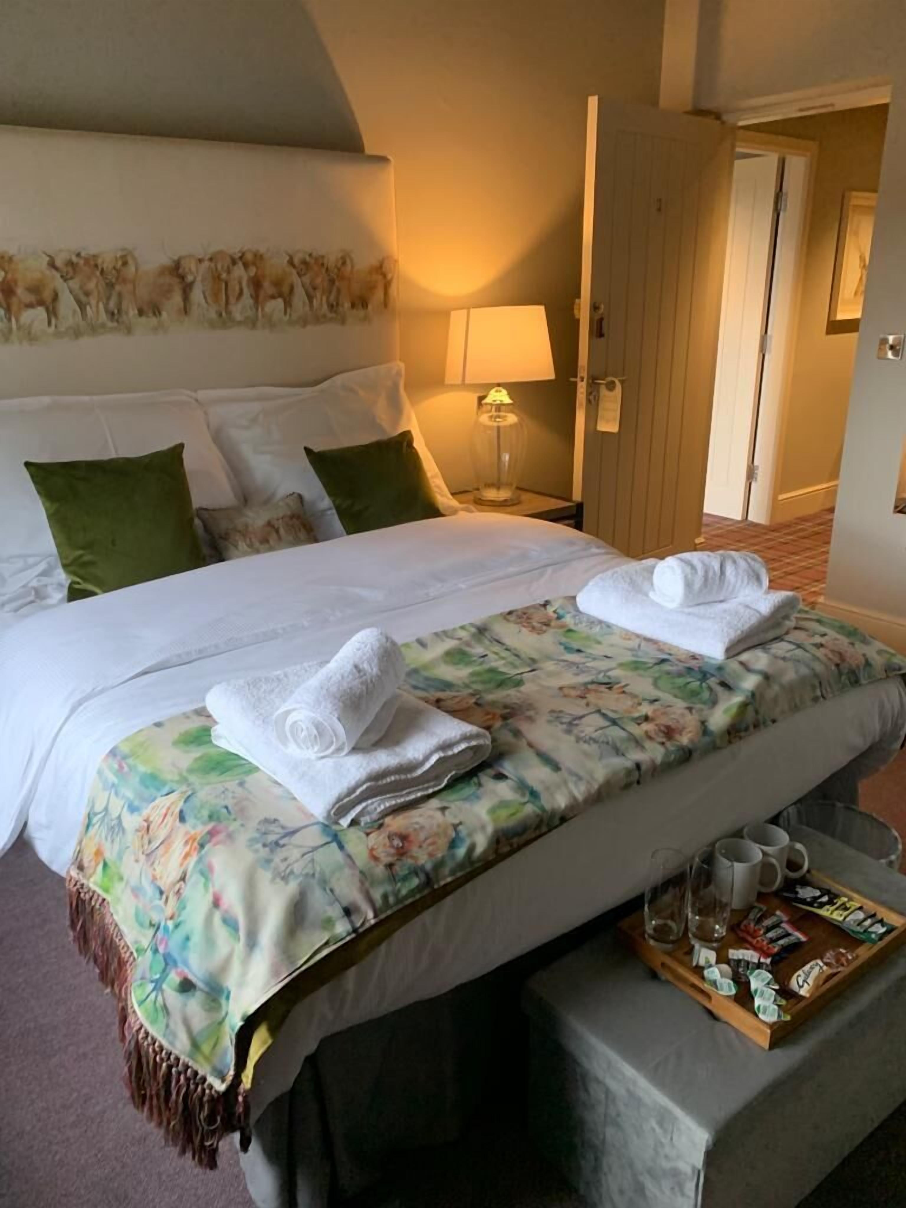 A hotel room with a bed, pillows, a bedside table with a lamp, and a tray with items.