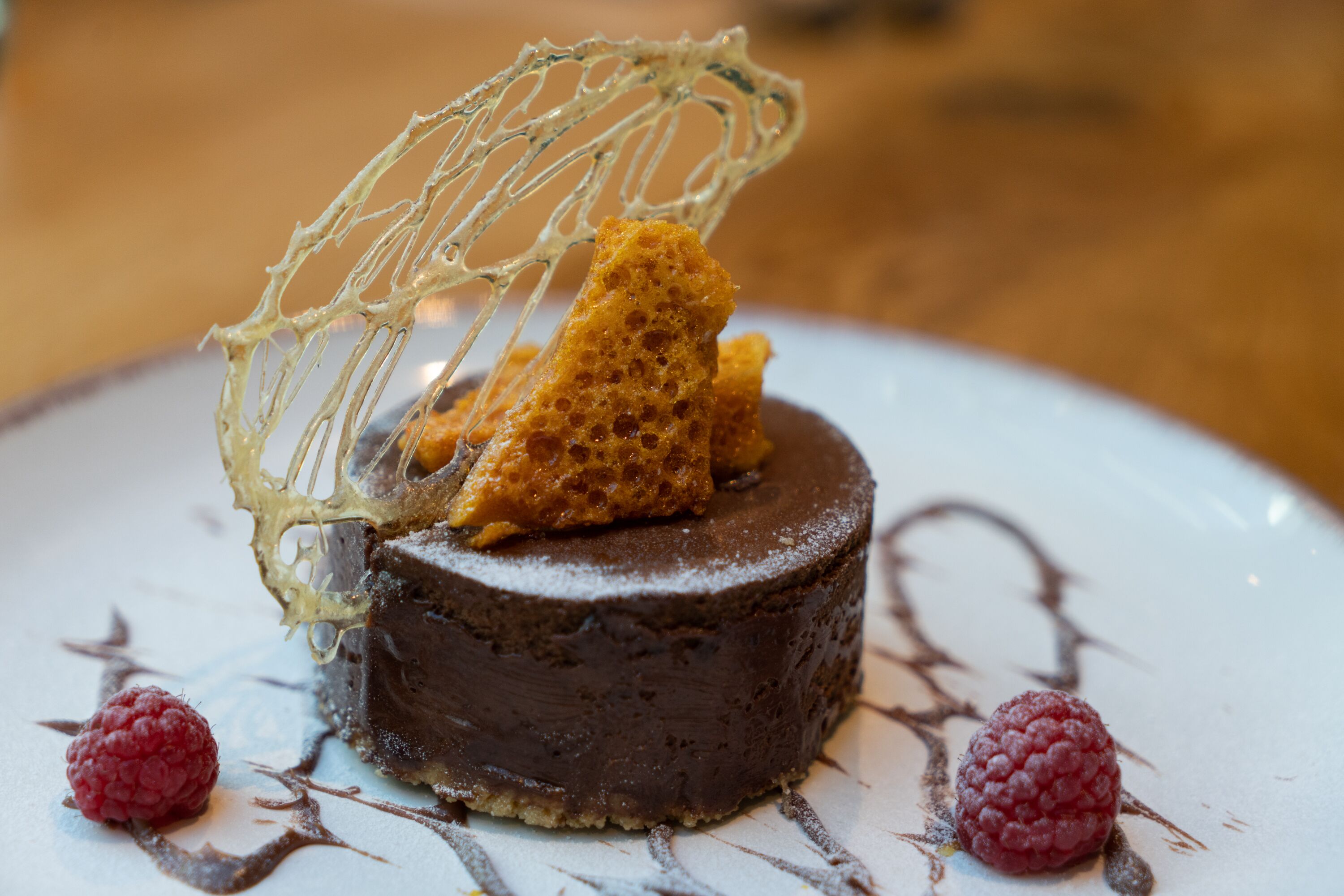 Un postre con base de chocolate, decoración de frambuesas y una red de azúcar decorativa.