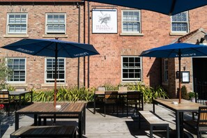 An outdoor patio area with wooden tables and blue umbrellas, brick walls, and a sign for 'Plum Partridge'.