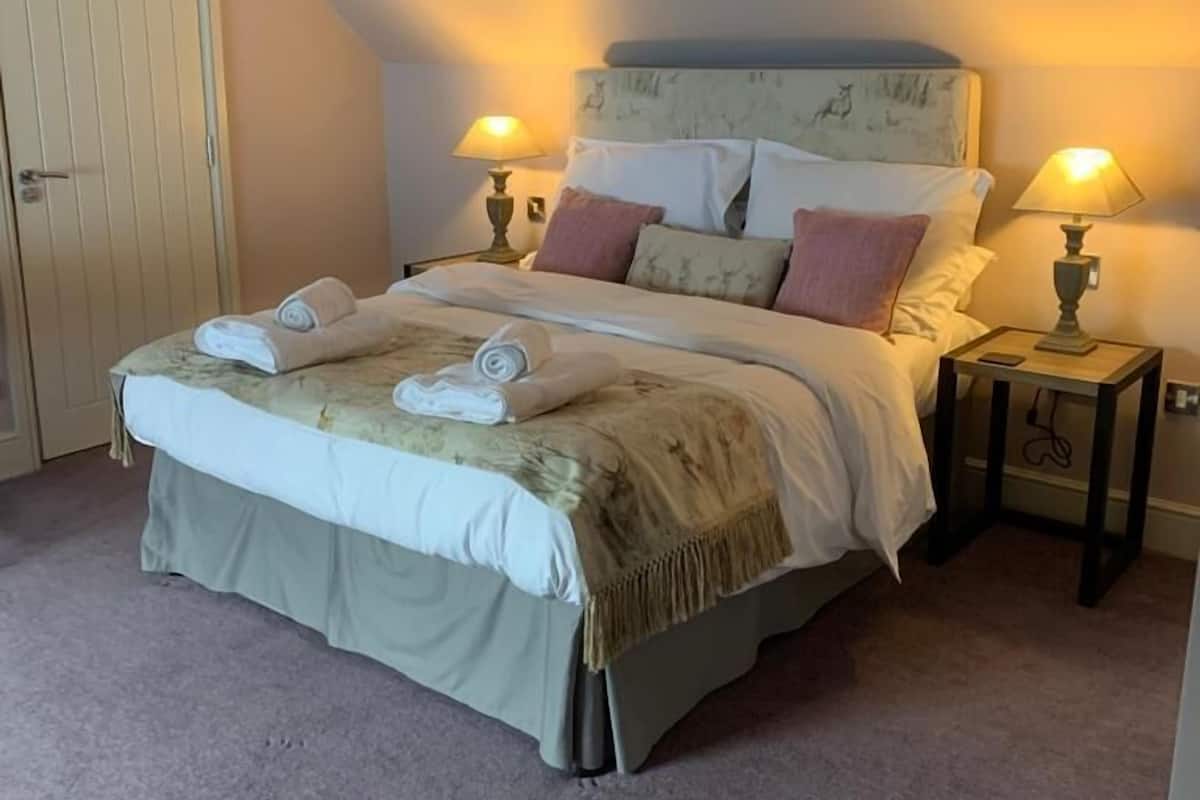 A neatly made bed with a headboard, two bedside tables with lamps, and a door to the left.