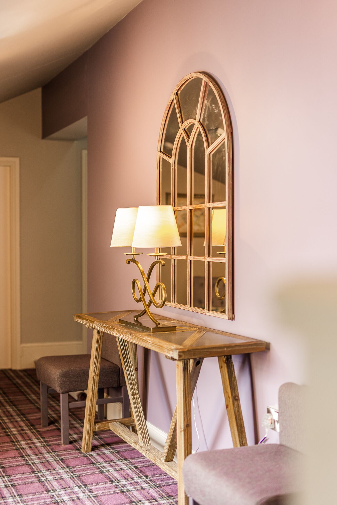 Una habitación con una mesa de madera, dos lámparas, un banco y un espejo junto a una ventana.