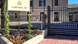 A gated entrance with a sign reading "GARDARELAIS" and a building with multiple windows and a balcony. - Garda Relais (Castelnuovo del Garda)