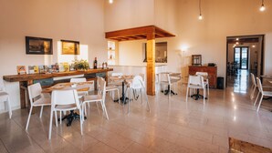 A spacious dining area with white chairs and a wooden table, featuring a high ceiling with exposed beams and pendant lighting. - Garda Relais (Castelnuovo del Garda)