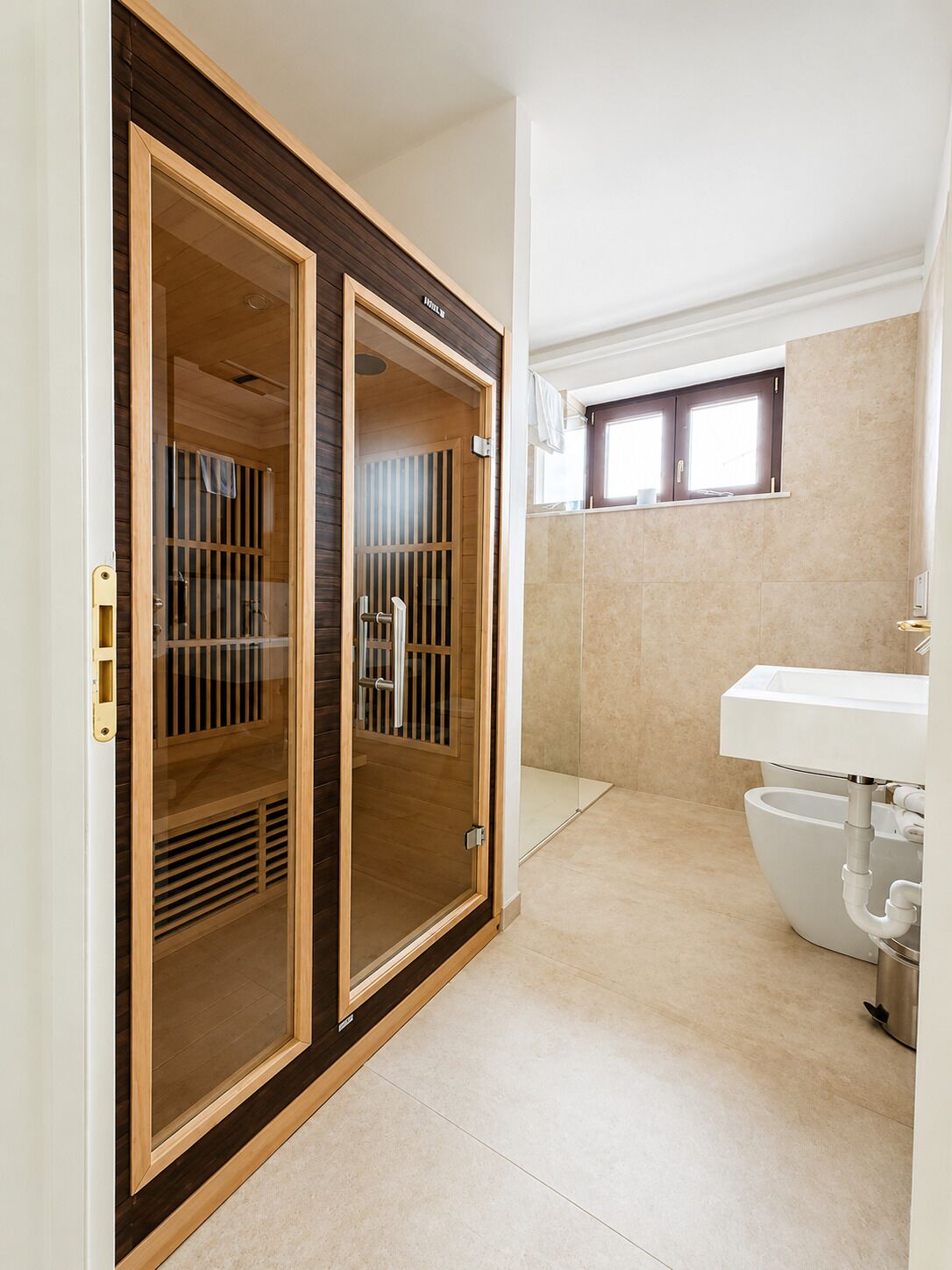 Un baño con ducha de vidrio, lavamanos y ventana sobre el espejo.