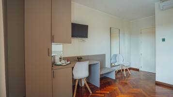 Ein modernes Hotelzimmer mit Holzboden im Fischgrätmuster, einer Küchenzeile mit Flachbildfernseher, einem großen Spiegel und einer Sitzecke mit weißem Stuhl.