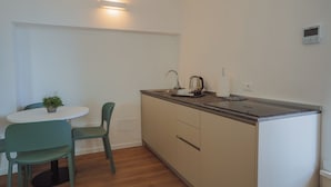 A compact kitchen with a white countertop, a sink, and a kettle. There is a small table with two chairs and a potted plant. - Garda Relais (Castelnuovo del Garda)