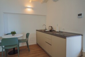 A compact kitchen with a white countertop, a sink, and a kettle. There is a small table with two chairs and a potted plant. - Garda Relais (Castelnuovo del Garda)