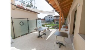 A balcony with a table and chairs, a glass door, and a view of a garden and buildings in the background. - Garda Relais (Castelnuovo del Garda)
