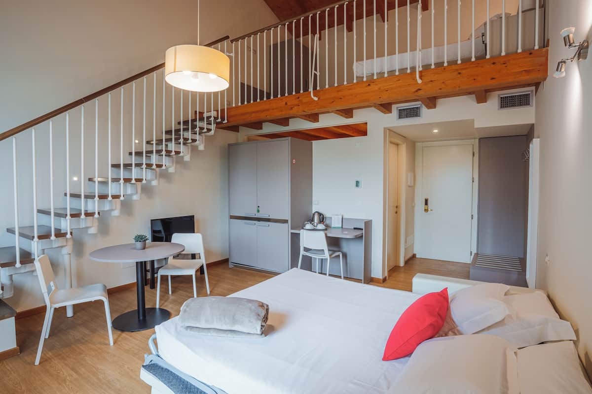A modern hotel room with a staircase, a desk, and a bed with pillows.
