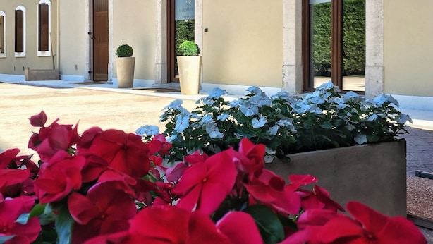 A building with a reception area, large windows, and a planter with red flowers. - Garda Relais (Castelnuovo del Garda)