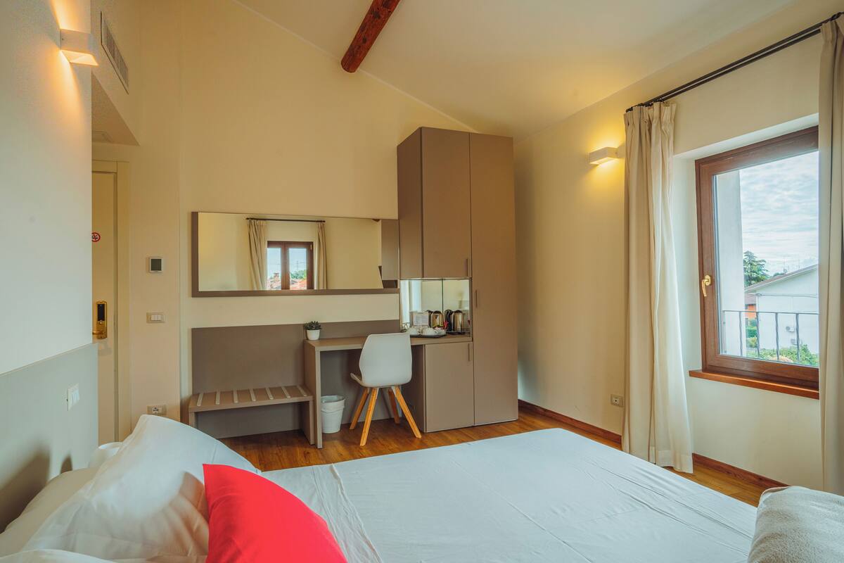 A bedroom with a bed, a desk, a chair, a wardrobe, and a window with curtains.